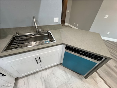 Kitchen with white cabinetry, light stone counters, dishwashing machine, and a peninsula