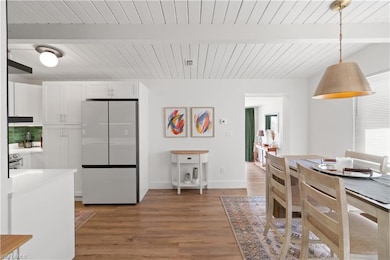 Kitchen with hardwood / wood-style flooring, refrigerator, white cabinetry, decorative light fixtures, and beamed ceiling
