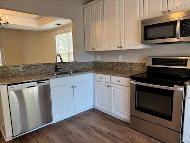 Kitchen with appliances with stainless steel finishes, white cabinetry, a tray ceiling, ornamental molding, and dark stone counters