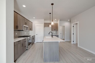 Kitchen featuring stainless steel appliances, decorative light fixtures, decorative backsplash, a kitchen island with sink, and light wood finished floors