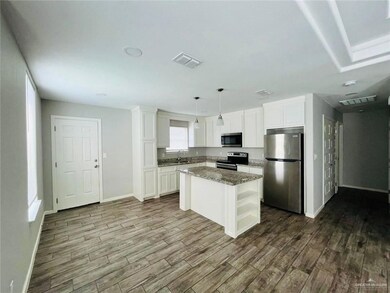 Kitchen with stainless steel appliances, dark wood-style flooring, white cabinets, and light stone counters
