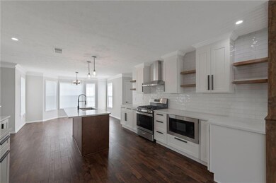 Kitchen with open shelves, appliances with stainless steel finishes, crown molding, wall chimney range hood, and backsplash