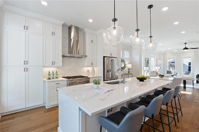 Kitchen featuring wall chimney range hood, high end appliances, light wood-type flooring, a center island with sink, and recessed lighting