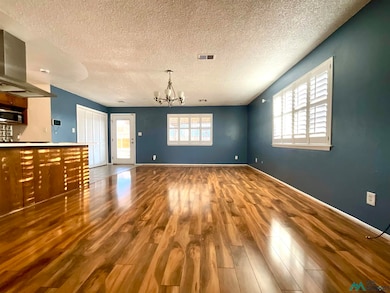 Unfurnished living room with a textured ceiling, dark wood-type flooring, and a chandelier