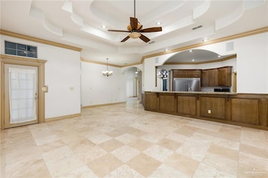 Unfurnished living room featuring light tile floors, a tray ceiling, ceiling fan with notable chandelier, and crown molding