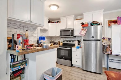 Kitchen featuring appliances with stainless steel finishes, backsplash, white cabinetry, crown molding, and light wood finished floors