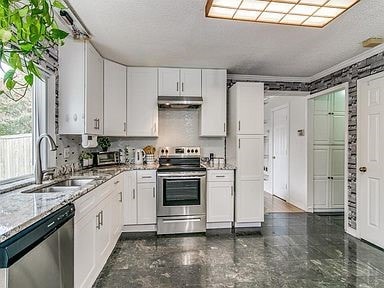 Kitchen with appliances with stainless steel finishes, white cabinets, light stone countertops, tasteful backsplash, and a textured ceiling
