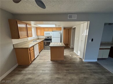 Kitchen featuring a textured ceiling, white appliances, a center island, dark wood-type flooring, and light stone countertops