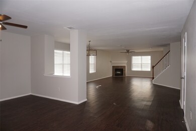 Unfurnished living room featuring ceiling fan, dark wood finished floors, a tiled fireplace, stairs, and a chandelier