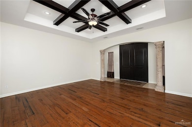Unfurnished living room featuring decorative columns, coffered ceiling, dark hardwood / wood-style floors, and ceiling fan