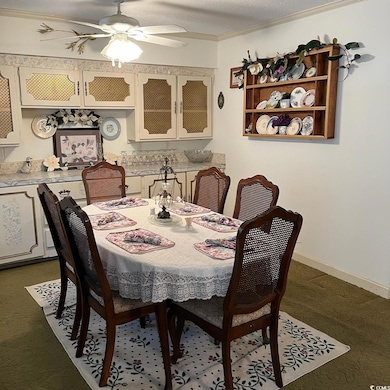 Dining room featuring ceiling fan, baseboards, dark colored carpet, and crown molding