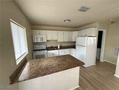Kitchen featuring a center island, sink, white appliances, white cabinets, and light wood-type flooring