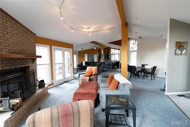 Living area with rail lighting, a brick fireplace, carpet floors, a chandelier, and lofted ceiling