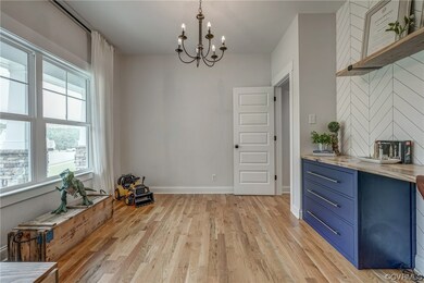 The office, which is a flex space that could be used for multiple uses, features a built-in desk/cabinet area. A lovely chandelier and large windows provide plenty of light. The door leads to a back hallway to the powder room and kitchen.