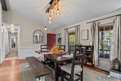 Dining space featuring crown molding, wood finished floors, vaulted ceiling, a wainscoted wall, and a chandelier