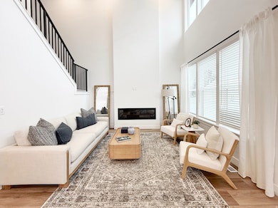 Living area with light wood-style flooring, a high ceiling, and a glass covered fireplace