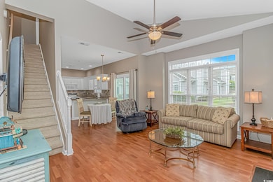 Living area with light wood-type flooring, a ceiling fan, a chandelier, vaulted ceiling, and stairway
