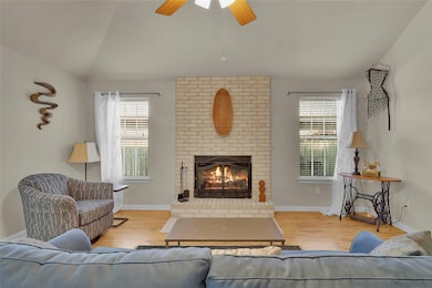 Living area featuring healthy amount of natural light, a fireplace, lofted ceiling, wood finished floors, and a ceiling fan
