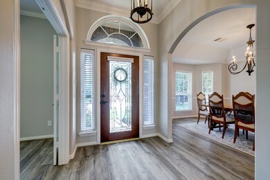 Step through a stunning wood and leaded glass door into this elegant entry featuring gorgeous vinyl plank flooring, arched doorways, and a soaring ceiling with thick crown molding and a stylish chandelier. The entry is flanked on one side by a private study and on the other, the formal dining room.