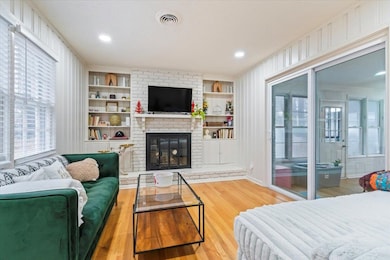 Living room featuring light wood-type flooring, built in features, and a fireplace
