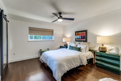 Bedroom featuring a barn door, ornamental molding, dark wood-style floors, and a ceiling fan