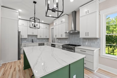 Kitchen with wall chimney exhaust hood, a chandelier, appliances with stainless steel finishes, a center island, and a sink