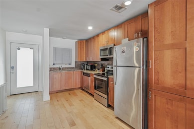 Kitchen with stainless steel appliances, light stone counters, light wood-type flooring, and backsplash