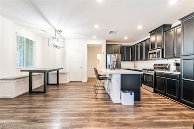 Kitchen featuring appliances with stainless steel finishes, decorative light fixtures, dark cabinetry, a breakfast bar area, and recessed lighting