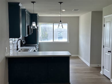 Kitchen featuring a sink, a peninsula, light wood finished floors, light countertops, and appliances with stainless steel finishes