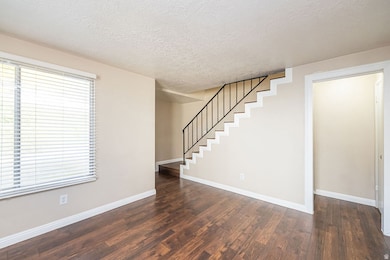 Unfurnished living room featuring a textured ceiling, stairway, and dark wood-type flooring