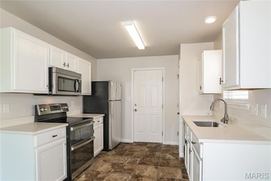 Kitchen with stainless steel appliances, white cabinetry, stone finish flooring, and light stone counters