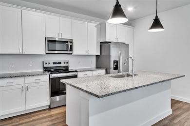 Kitchen featuring dark wood finished floors, stainless steel appliances, white cabinets, a sink, and an island with sink