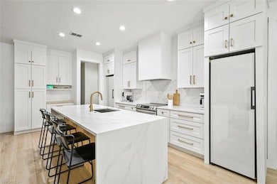 Kitchen with fridge, a sink, stainless steel electric range, custom exhaust hood, and a kitchen bar