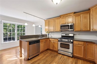 Kitchen with appliances with stainless steel finishes, a peninsula, hanging light fixtures, dark stone counters, and light wood-style floors