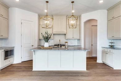 Kitchen with light stone countertops, decorative backsplash, decorative light fixtures, a kitchen island with sink, and recessed lighting