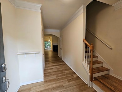 Corridor with arched walkways, ornamental molding, light wood-type flooring, and stairs