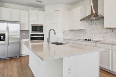 Kitchen featuring appliances with stainless steel finishes, wall chimney range hood, tasteful backsplash, and white cabinets