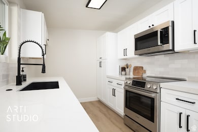 Kitchen with backsplash, stainless steel appliances, and white cabinetry