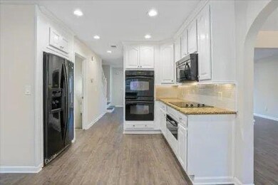 Kitchen featuring arched walkways, baseboards, backsplash, white cabinetry, and black appliances