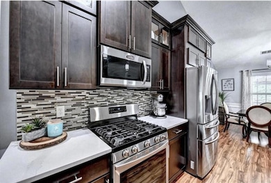 Kitchen featuring appliances with stainless steel finishes, tasteful backsplash, light countertops, light wood-style floors, and dark brown cabinetry
