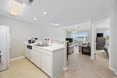 Kitchen with a sink, white appliances, a peninsula, a ceiling fan, and a textured ceiling