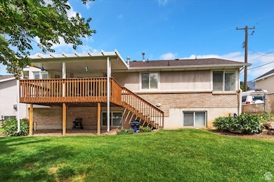Back of property with brick siding, stairway, a wooden deck, a patio area, and a yard
