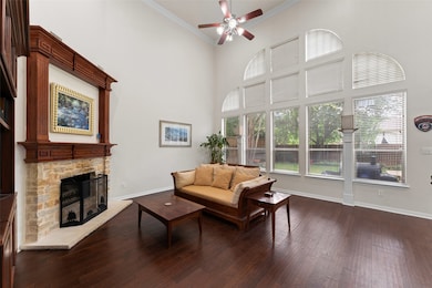Living area featuring a ceiling fan, dark wood-style flooring, a stone fireplace, ornamental molding, and a high ceiling