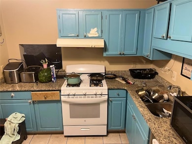 Kitchen featuring white gas stove, under cabinet range hood, and blue cabinetry