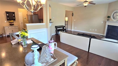 Dining room featuring dark wood-style flooring, a chandelier, a ceiling fan, a fireplace with flush hearth, and baseboards