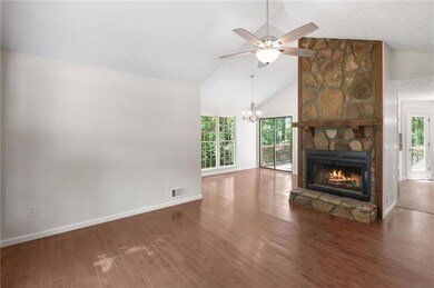 Unfurnished living room with a stone fireplace, a chandelier, a ceiling fan, wood finished floors, and high vaulted ceiling
