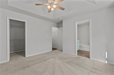 Primary bedroom featuring a spacious closet, light carpet, a raised ceiling, ensuite bath, and ceiling fan