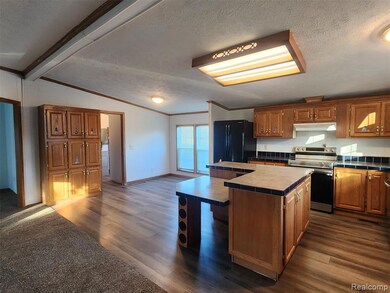 Kitchen featuring a textured ceiling, tile counters, stainless steel electric range oven, a kitchen island, and brown cabinets