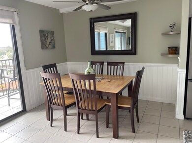 Dining room with a ceiling fan, a wainscoted wall, and light tile patterned floors