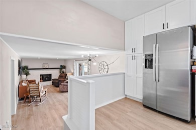 Kitchen with stainless steel fridge with ice dispenser, light wood-style floors, white cabinetry, and a fireplace